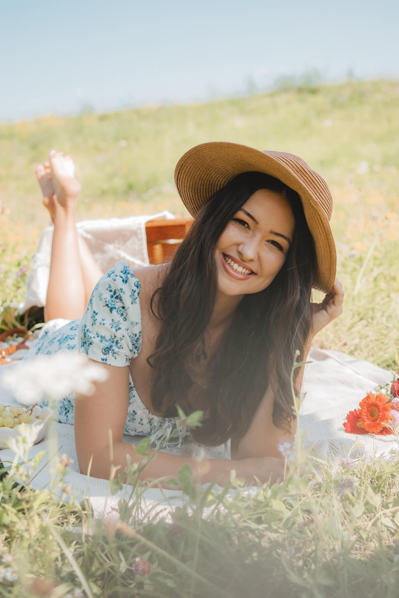 Junge Frau liegt mir einem Hut auf einer Picknickdecke im Grünen