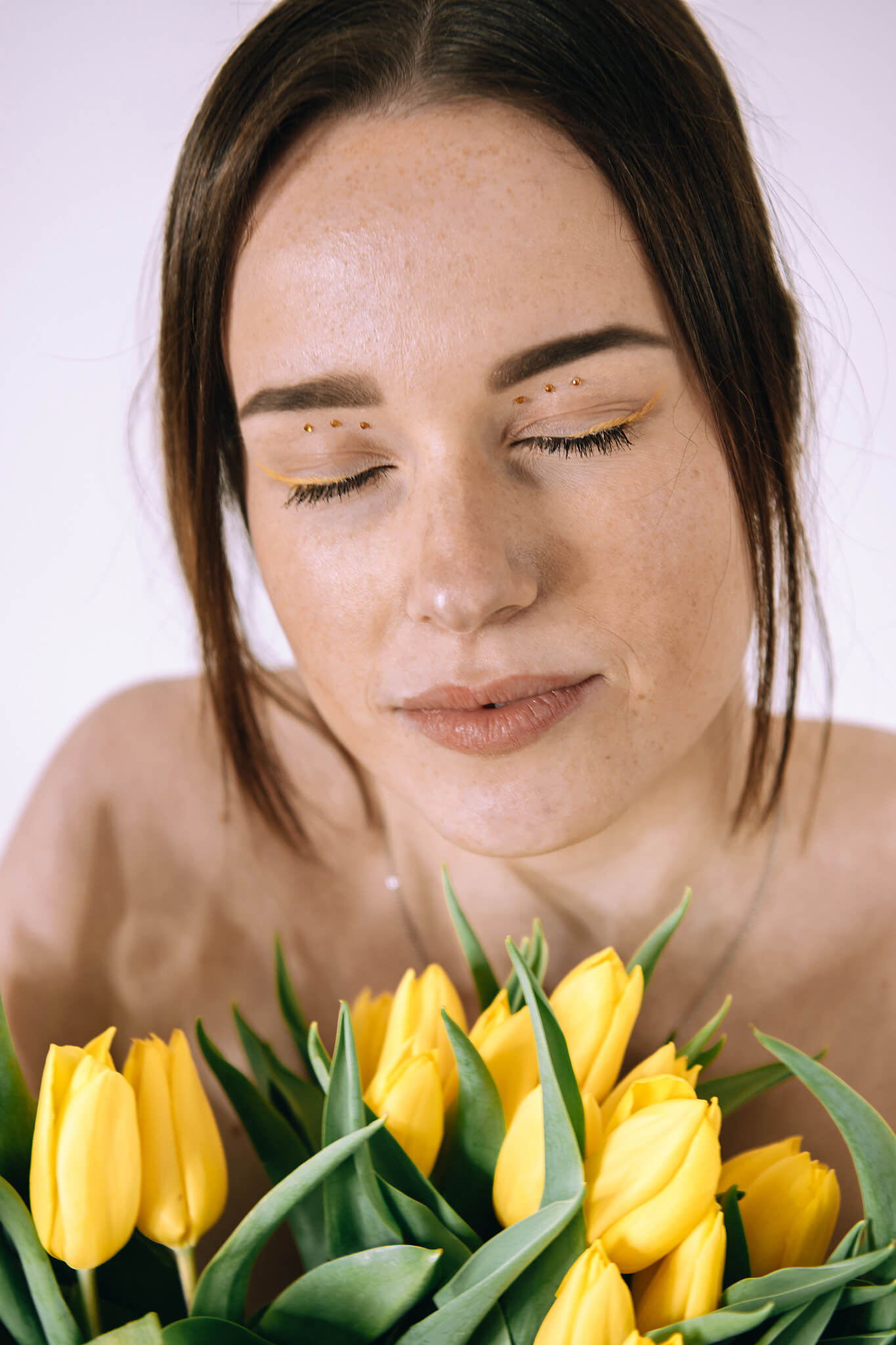 Dunkelhaarige, junge Frau mit gelbem Tulpen vor ihrem Oberkörper