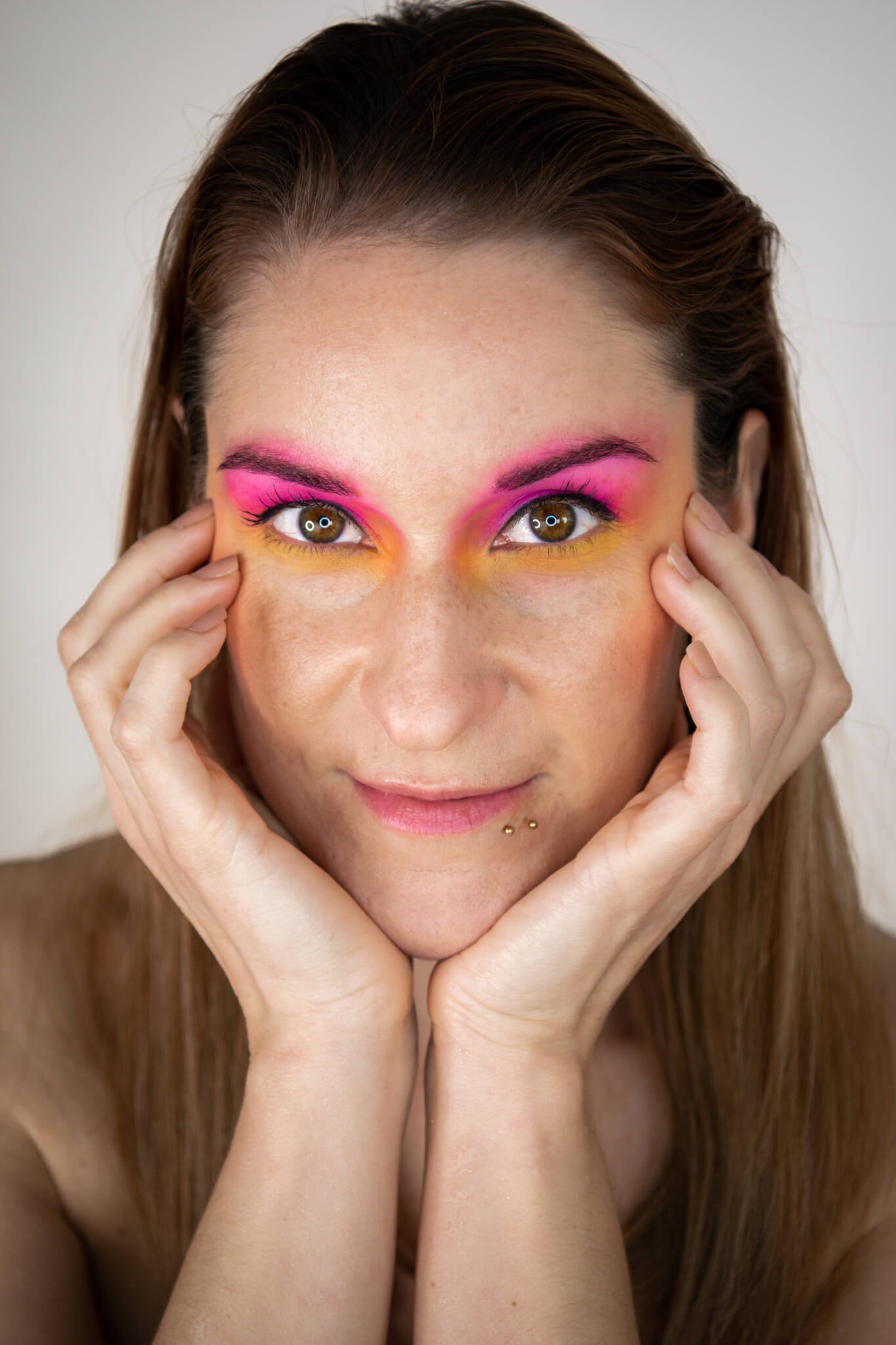 Rothaarige, junge Frau mit orange-pinken Augenmakeup vor weißem Hintergrund